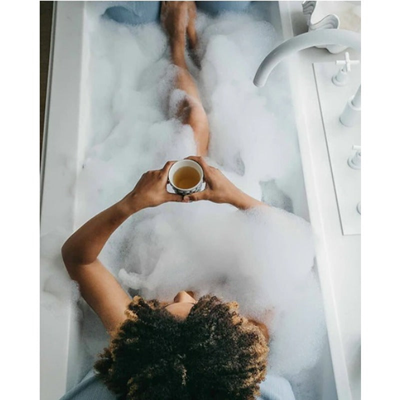 Person genießt Tee in der Badewanne mit Schaum – Selfcare-Moment mit Badesofa Kissen